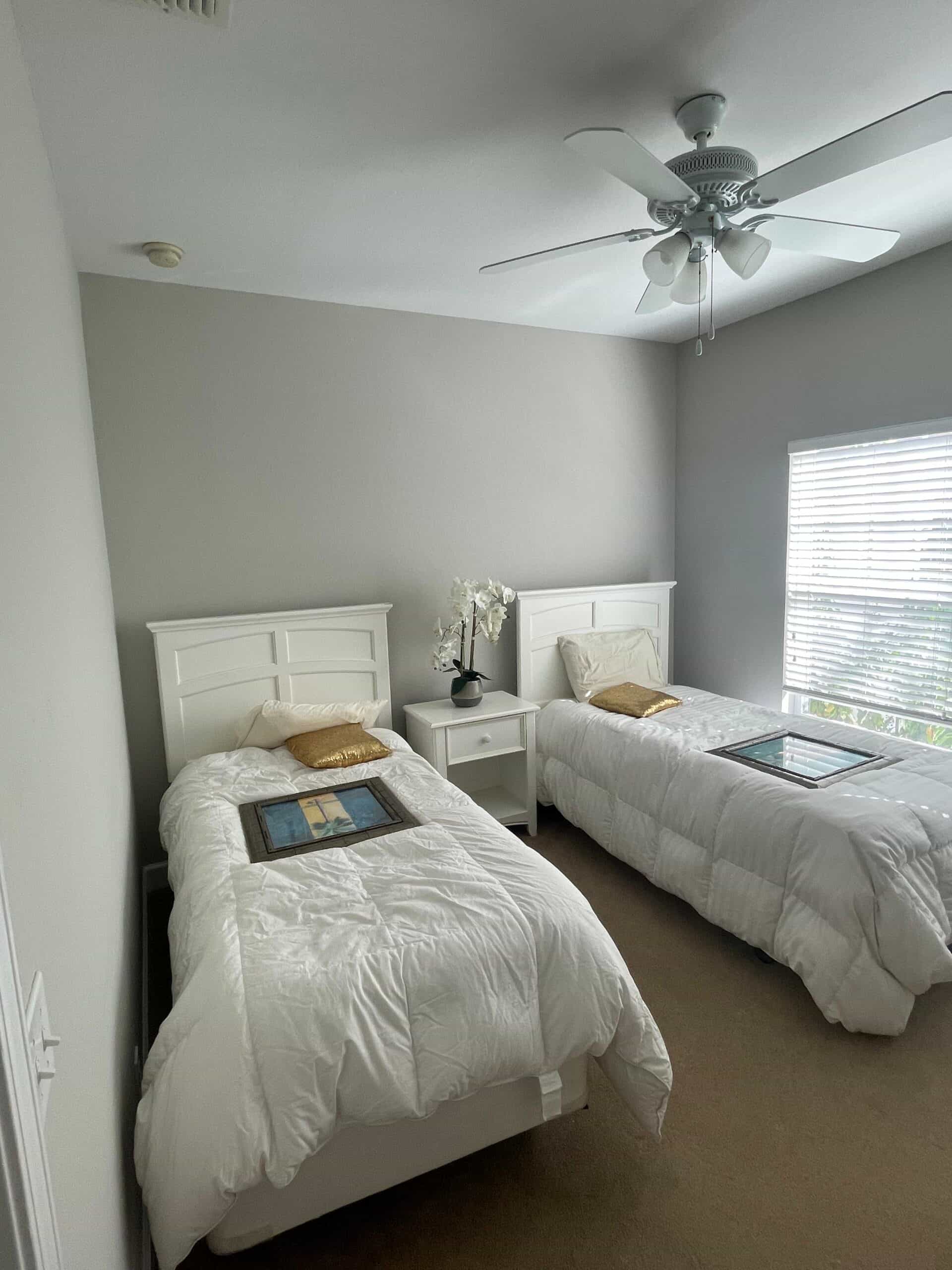Repainted twin bedroom in soft gray with white furniture and a ceiling fan