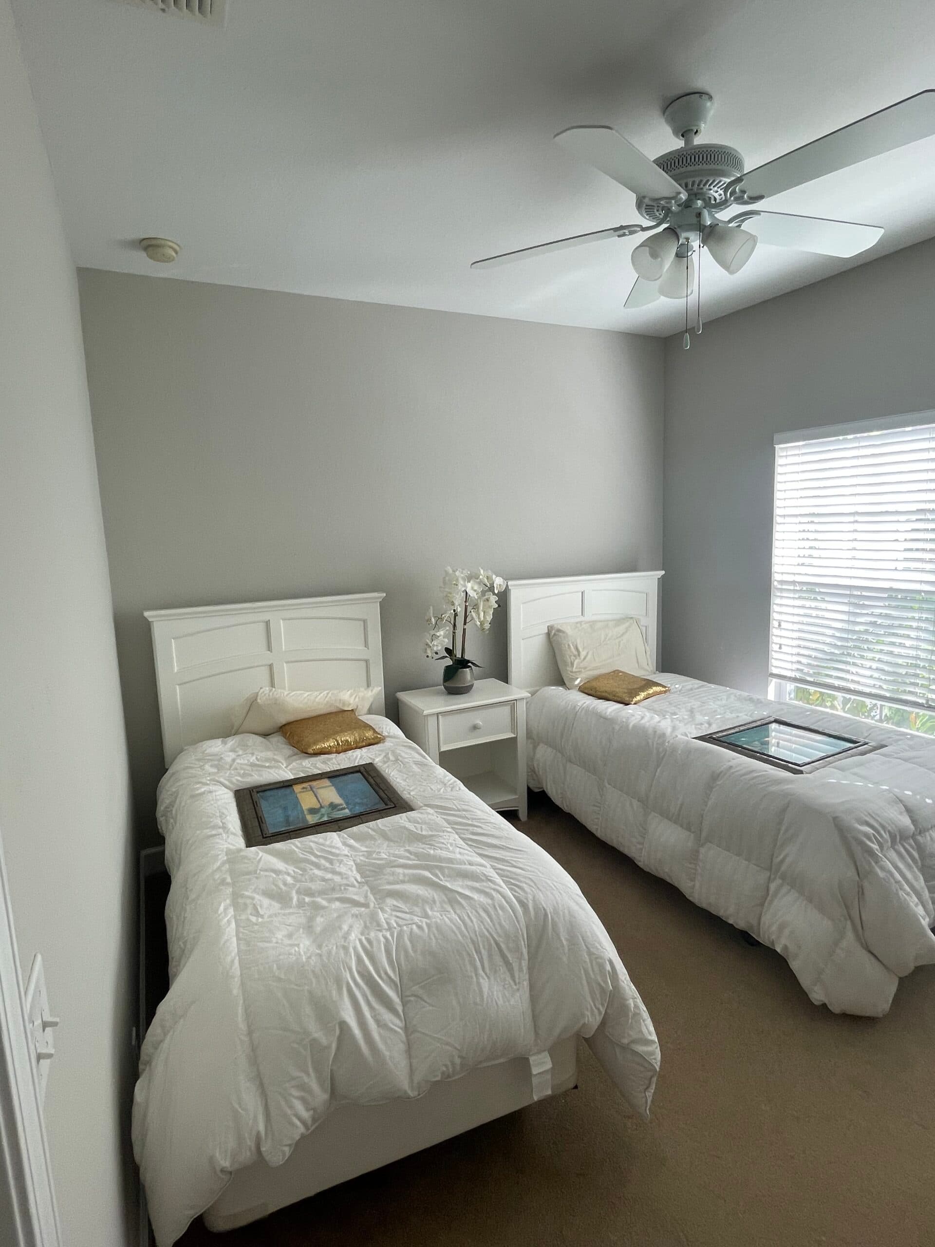 Repainted twin bedroom in soft gray with white furniture and a ceiling fan