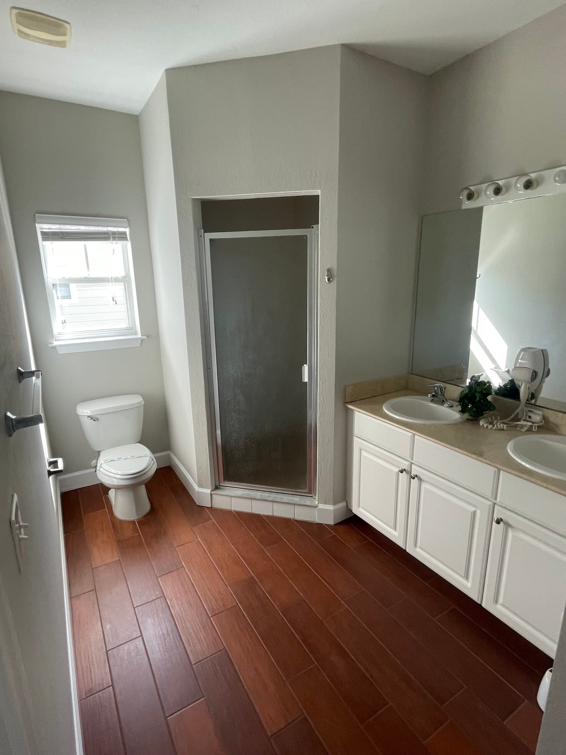 Repainted bathroom in soft gray with a white double vanity and wood-look tile floor