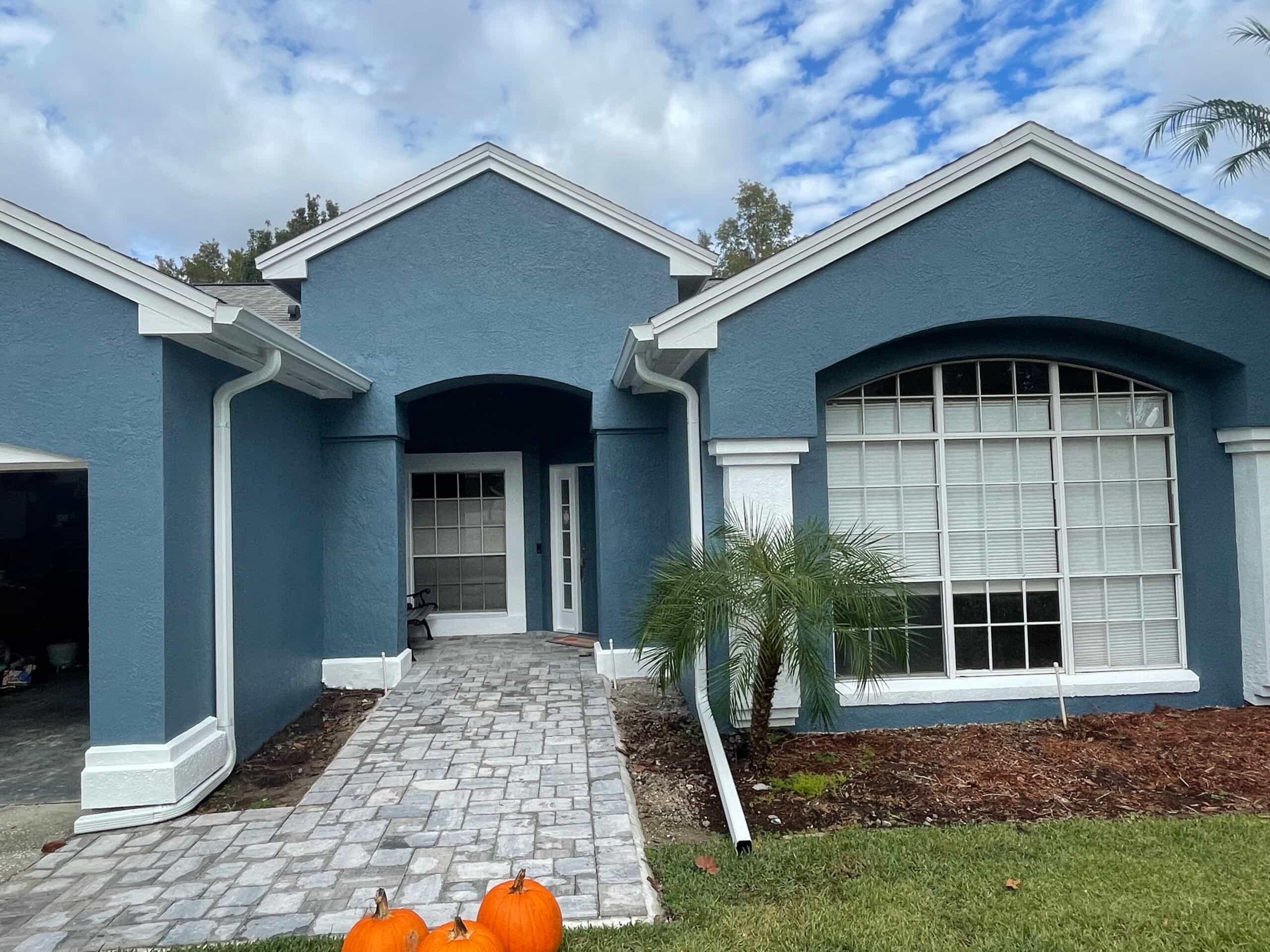Blue-gray stucco exterior with fresh white trim and a paver walkway after a full repaint and seal