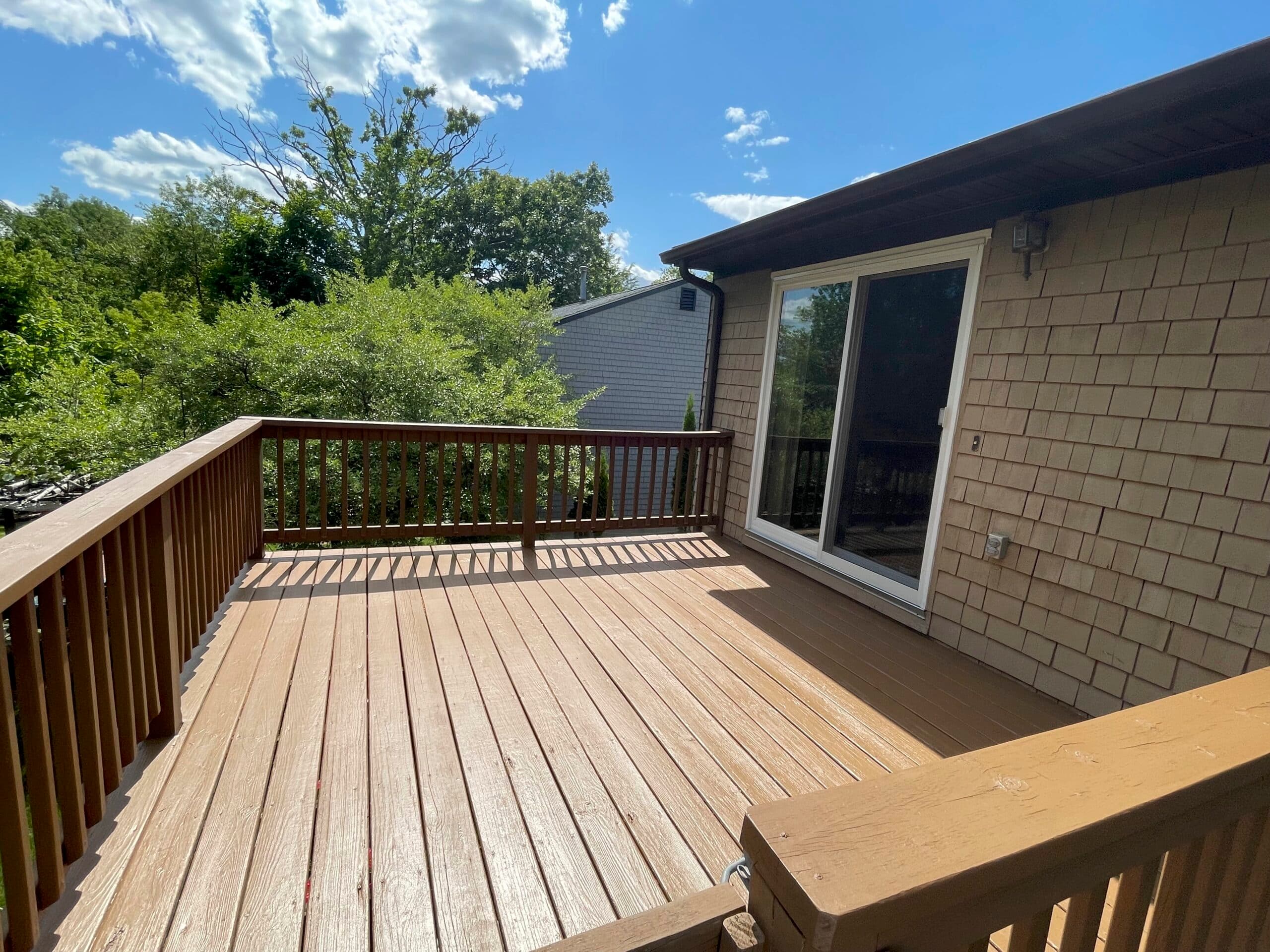 Refinished backyard deck with an even stain on boards and railings beside a shingled wall