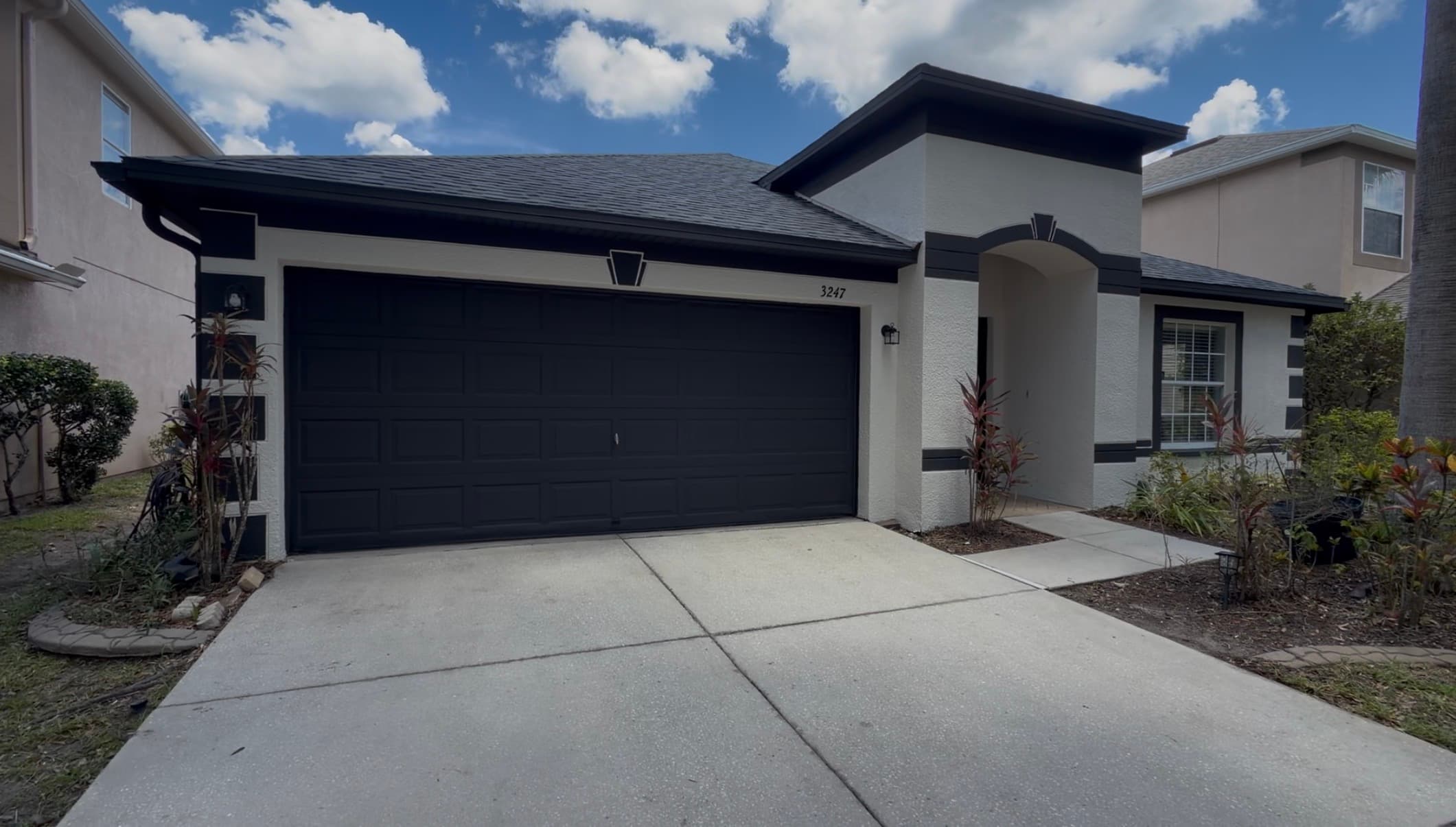 Single-story stucco home repainted crisp white with bold black trim, black garage door, and black keystone accents